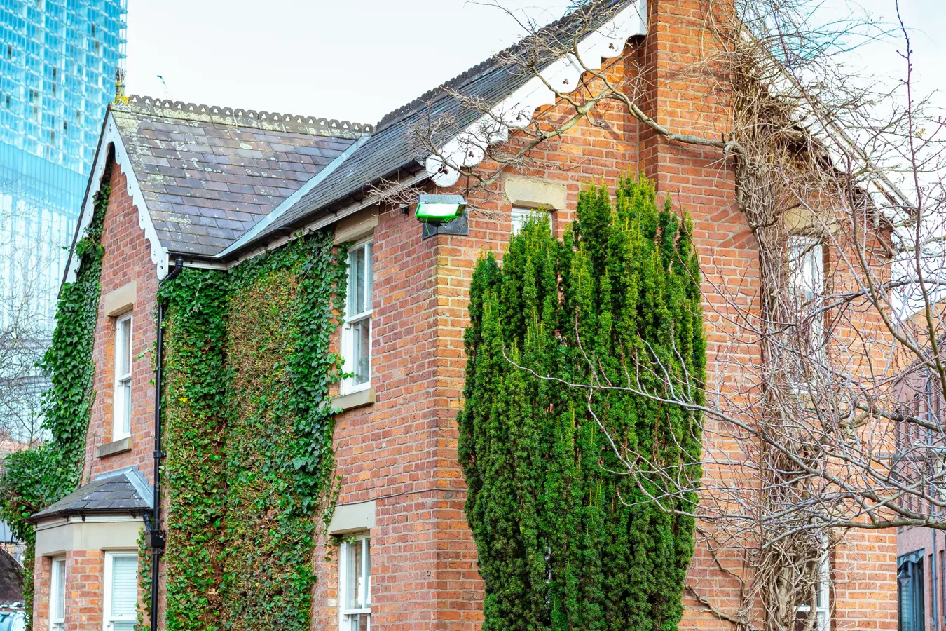 A red-brick cottage in front of a glass tower in Manchester